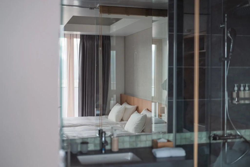 Blick durch Glaswand ins Schlafzimmer mit Doppelbetten und Vorhängen