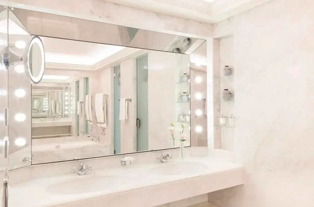 Modernes Badezimmer in hellem Marmor mit großen Spiegeln und elegantem Waschbereich.