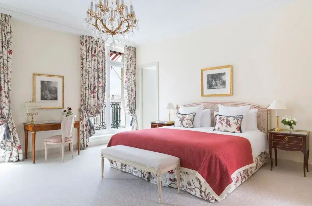 Elegantes Hotelzimmer mit rotem Überwurf auf einem Doppelbett und kristallfarbenem Kronleuchter.