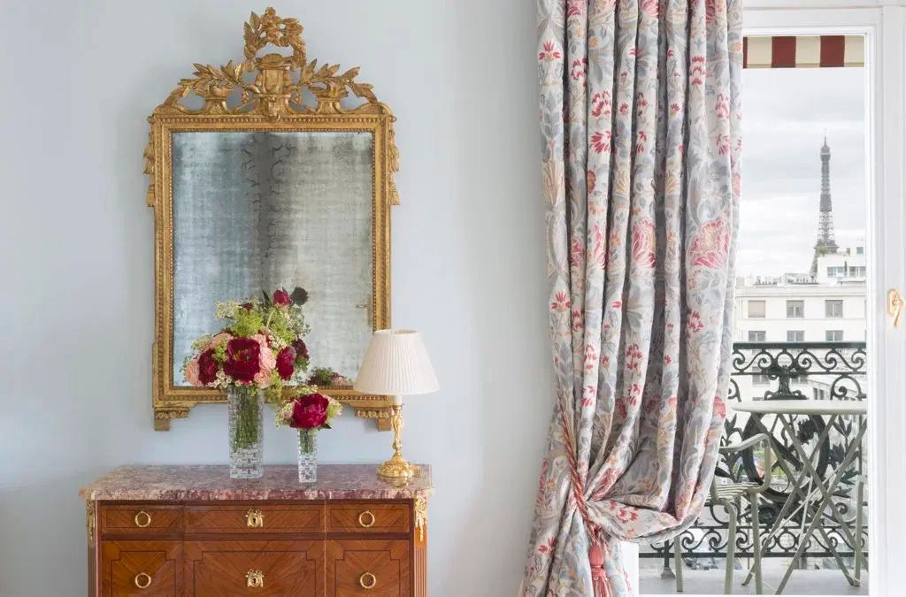Verzierte goldene Spiegelkommode mit Blumenarrangement und schweren Vorhängen.