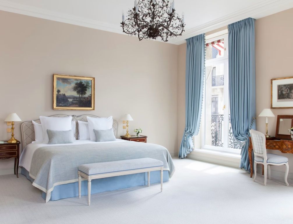 Suite mit Doppelbett, klassischem Gemälde und stilvollen blauen Vorhängen.