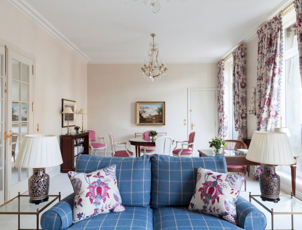 Wohnbereich mit blauer Couch, floralem Dekor und Kronleuchter.