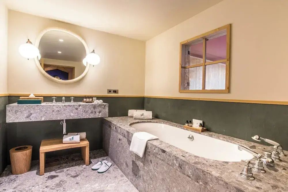 Luxuriöses Badezimmer mit großer Steinbadewanne und rundem Spiegel im Hotel Le Coucou Méribel