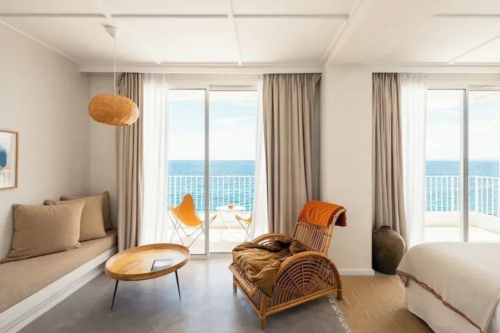 Wohnbereich der Suite mit Rattanmöbeln und Zugang zu einem Balkon mit Meerblick