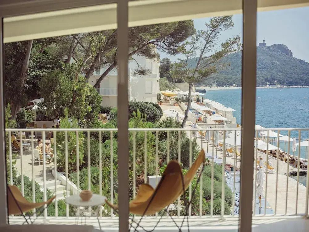 Blick vom Balkon des Hotels auf einen Garten mit Meer und Pinien im Hintergrund