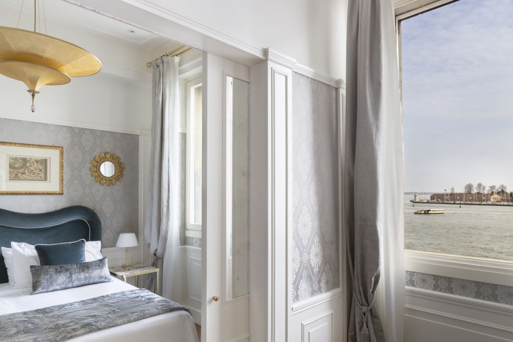 Helles Zimmer mit Doppelbett und Ausblick auf eine Lagune durch ein großes Fenster