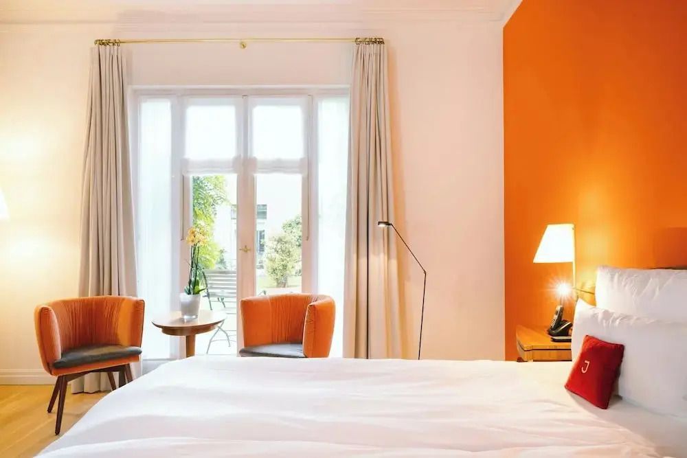 Hell eingerichtetes Deluxe Doppelzimmer mit Balkon und orangefarbenen Akzenten