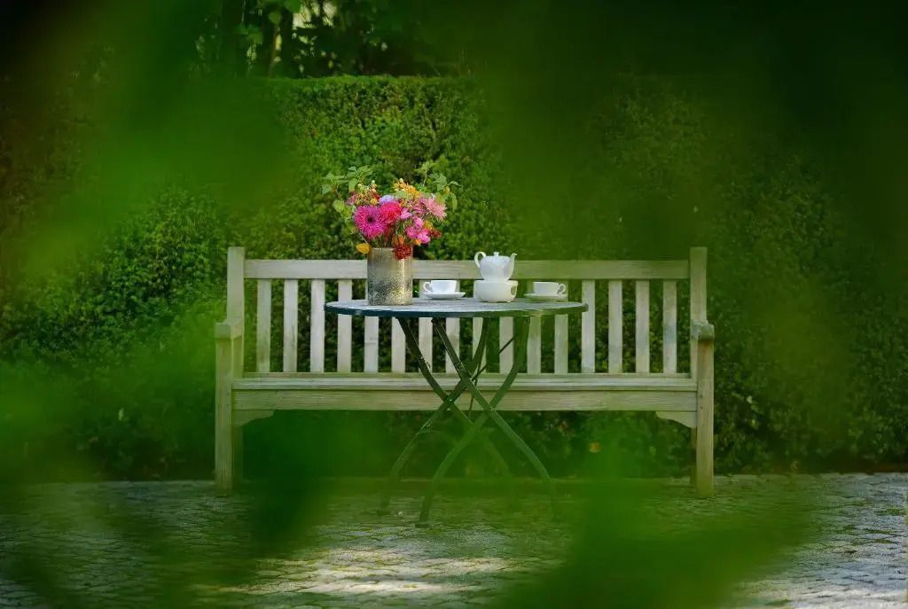 Gemütliche Gartenbank mit Blumenstrauß und Teeservice im Grünen.