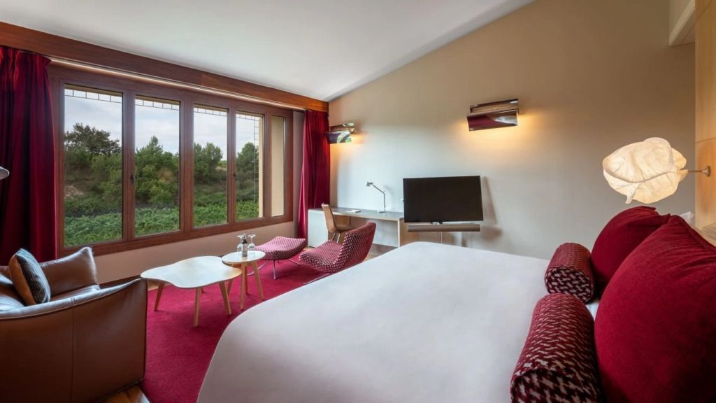 Modernes Hotelzimmer mit großem Fenster, Doppelbett und Sitzbereich in warmen Tönen.