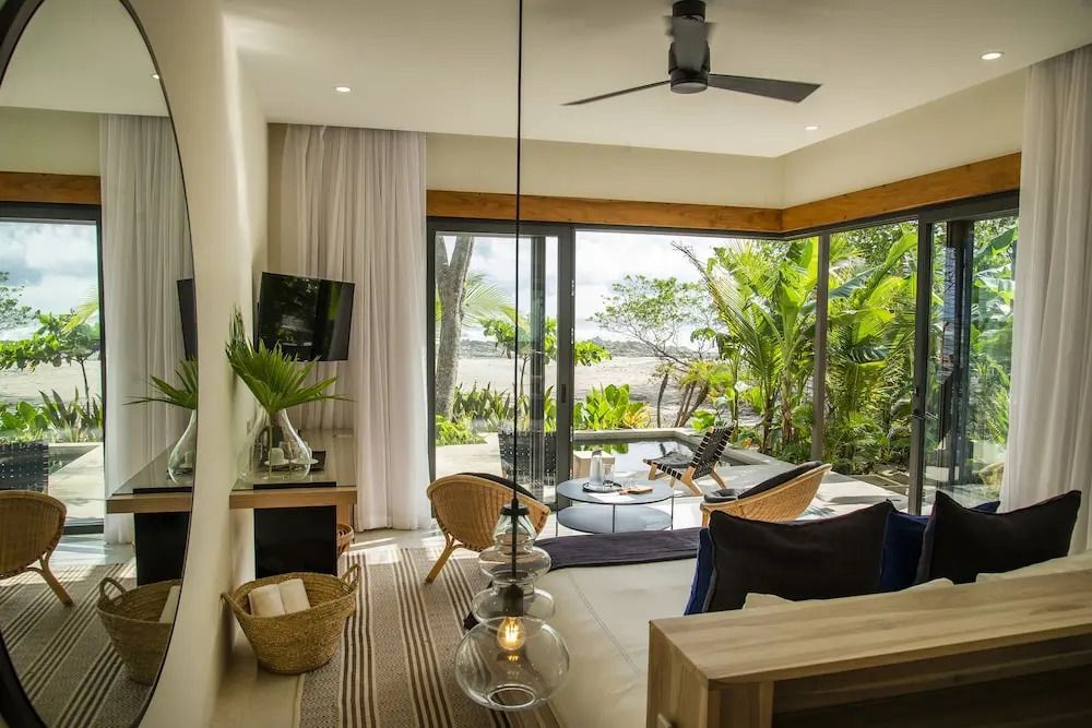 Helles Wohnzimmer mit großem Fenster und Blick auf den tropischen Garten.