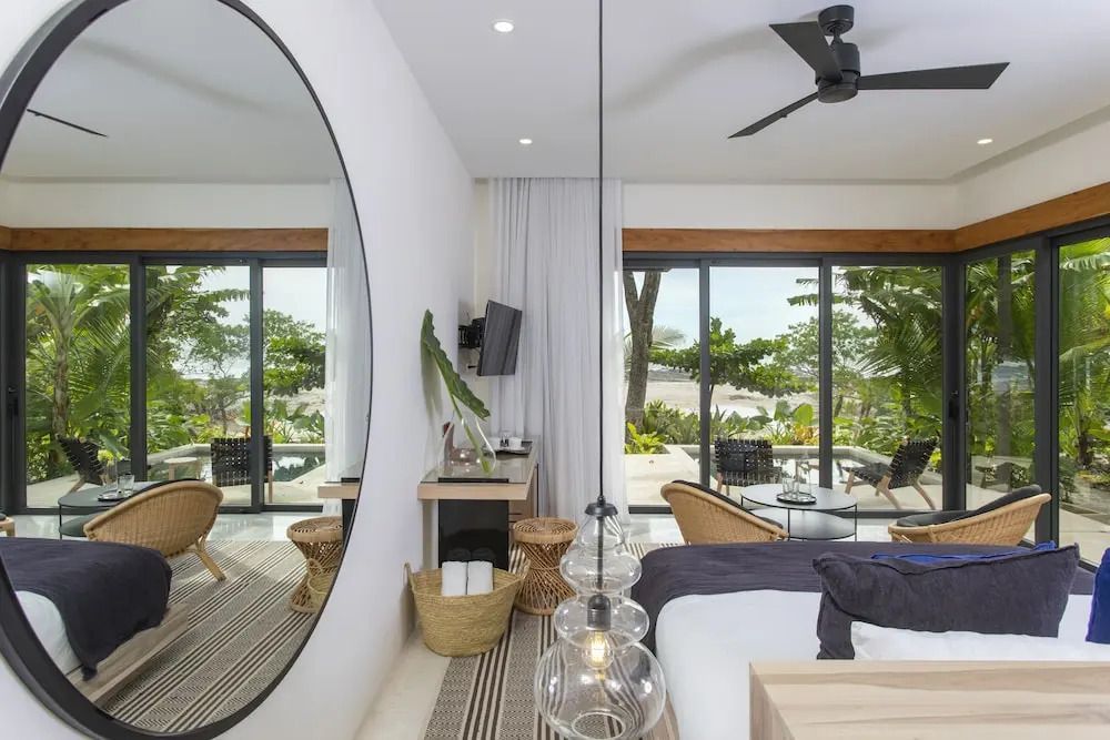 Zimmer mit Bett, großem Spiegel und Blick auf den tropischen Garten.