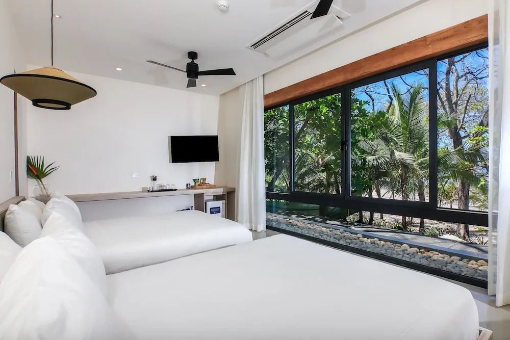 Helles Schlafzimmer mit zwei Betten und Aussicht auf grüne Vegetation.