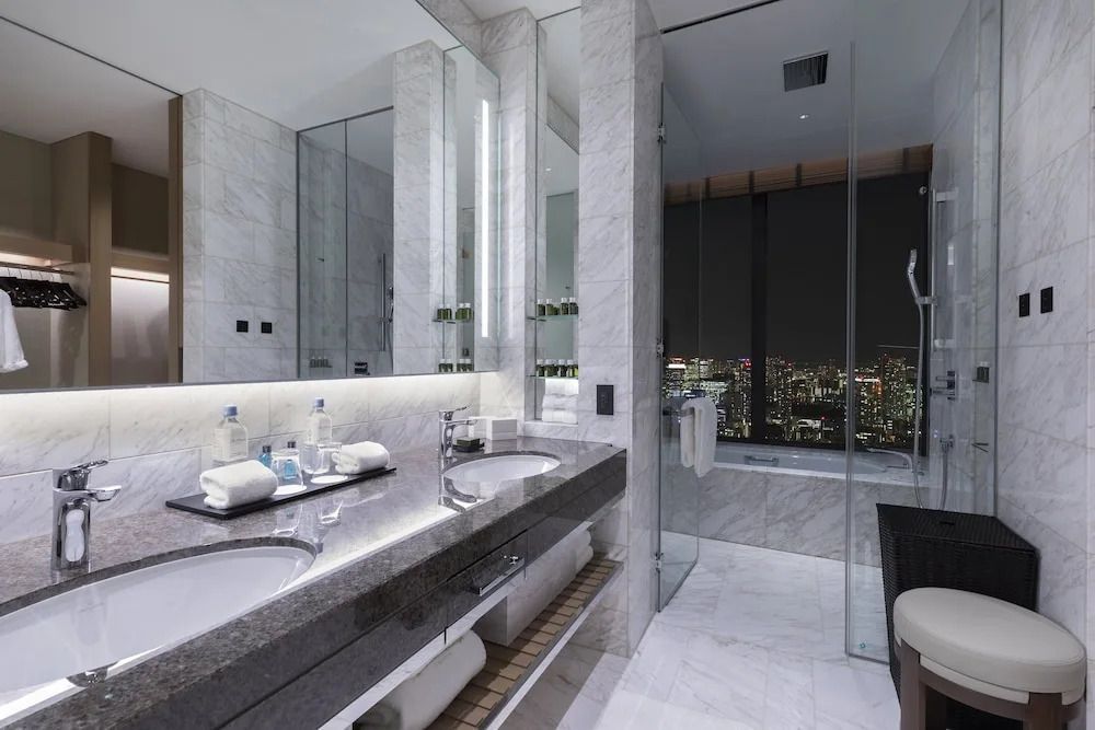 Modernes Badezimmer mit Marmoroberflächen und Blick auf die beleuchtete Stadtlandschaft.