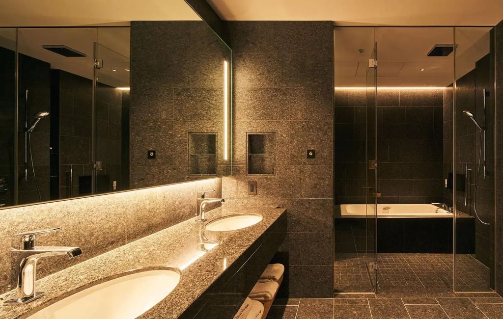 Luxuriöses Badezimmer in dunklem Stein mit Doppelwaschbecken und beleuchtetem Spiegel