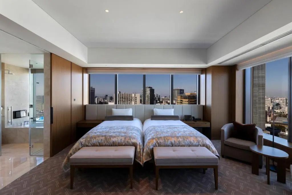 Zimmer mit zwei Betten und großen Fenstern mit Blick auf die Stadtlandschaft.