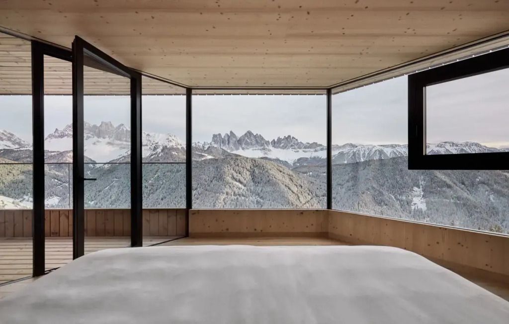 Schlafzimmer mit direktem Blick auf verschneite Dolomiten durch raumhohe Fenster
