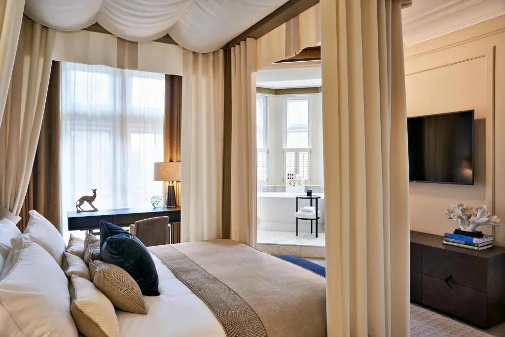 Helles Schlafzimmer mit eleganten Vorhängen und einem großen Doppelbett vor großen Fenstern.