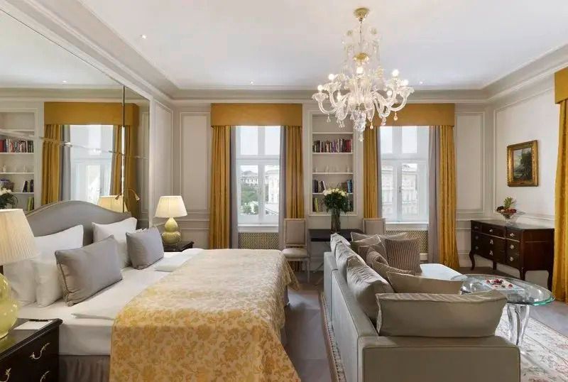 Elegante Suite mit Doppelbett, Sofa, Kronleuchter und Fenstern mit gelben Vorhängen