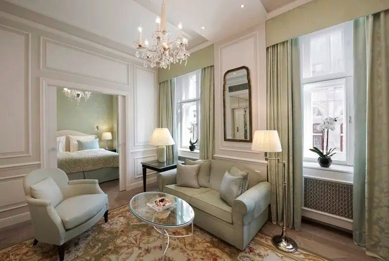 Wohnbereich der Suite mit Sofa, Sesseln, Kronleuchter und großen Fenstern