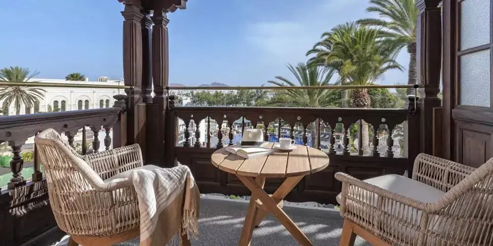 Gemütlicher Balkon mit Tisch und Stühlen, Blick auf Palmen und blauen Himmel