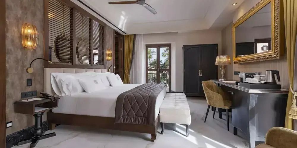 Elegantes Schlafzimmer mit Doppelbett, gemütlichen Sesseln und Blick auf Palmen.