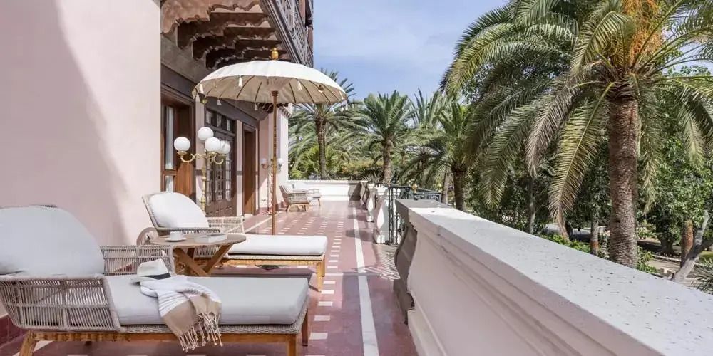 Geräumiger Balkon mit komfortablen Liegen und Sonnenschirmen, umgeben von Palmen.