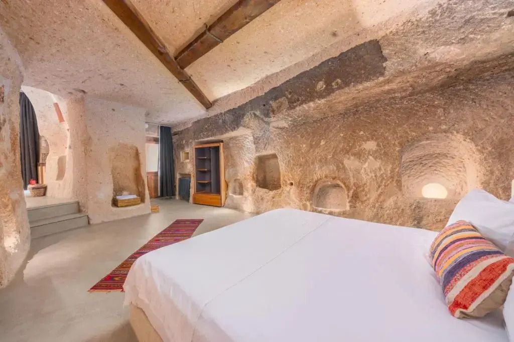 Großzügige Höhlensuite mit Doppelbett und Steinwänden, gemütlicher Teppich am Boden