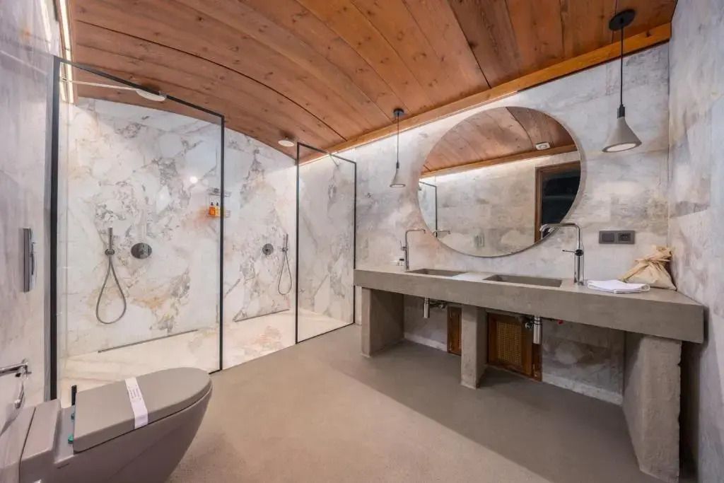 Modernes Badezimmer mit großen Marmorglasduschen und kreisförmigem Spiegel