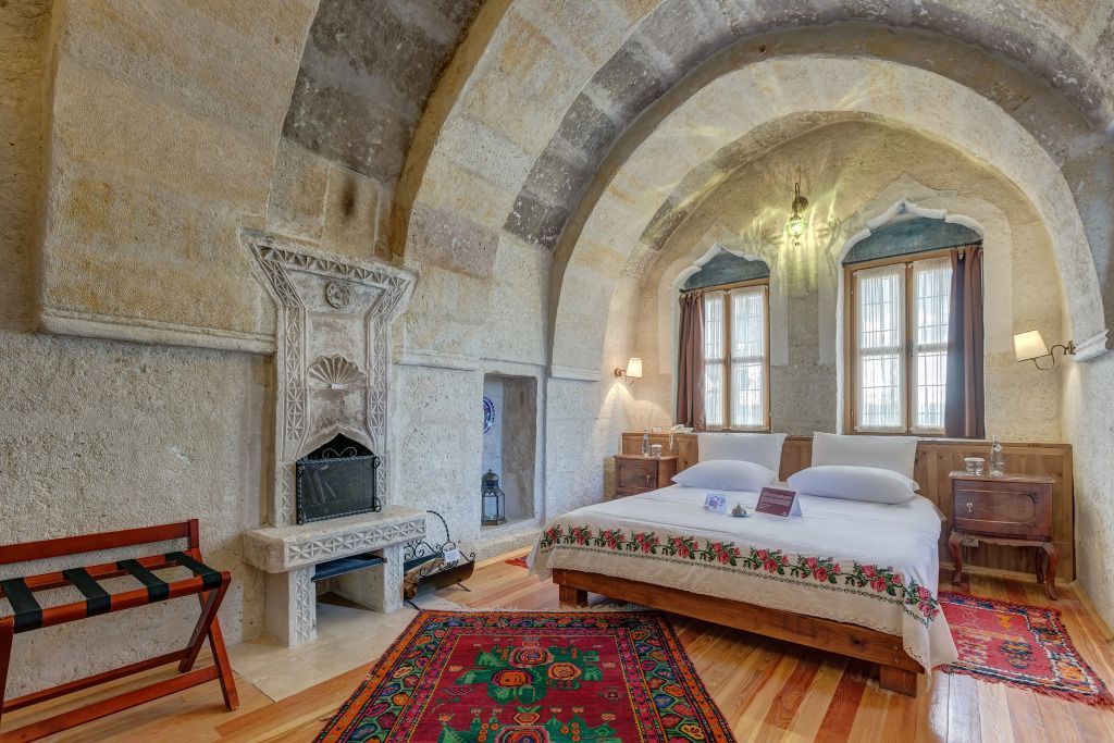 Steinwände, gewölbte Decke, Kamin, Doppelbett mit traditionellem Teppich im Hotelzimmer