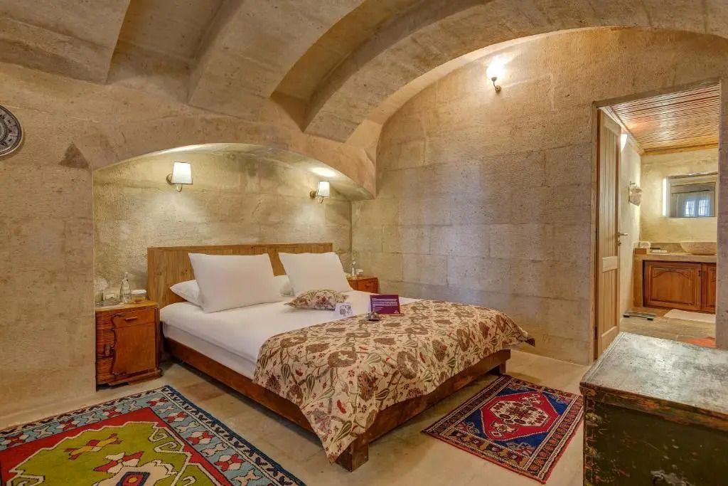 Zimmer mit steinener Gewölbedecke, gemütlichem Bett und bunten Teppichen