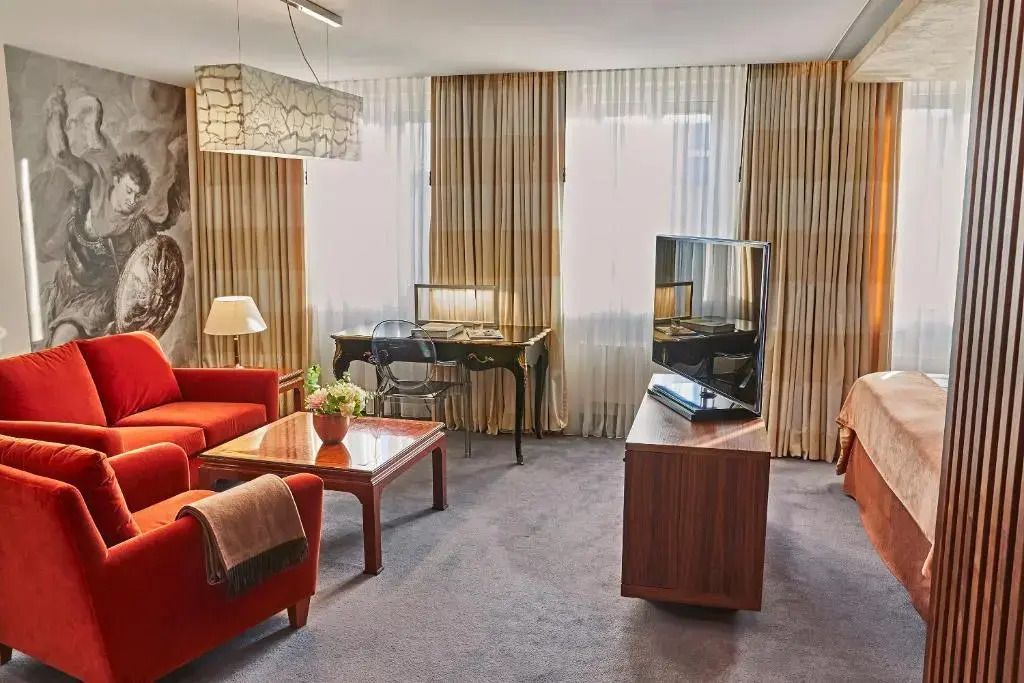 Helles Wohnzimmer mit stilvollem Sofa, Schreibtisch und Fernseher am Fenster.