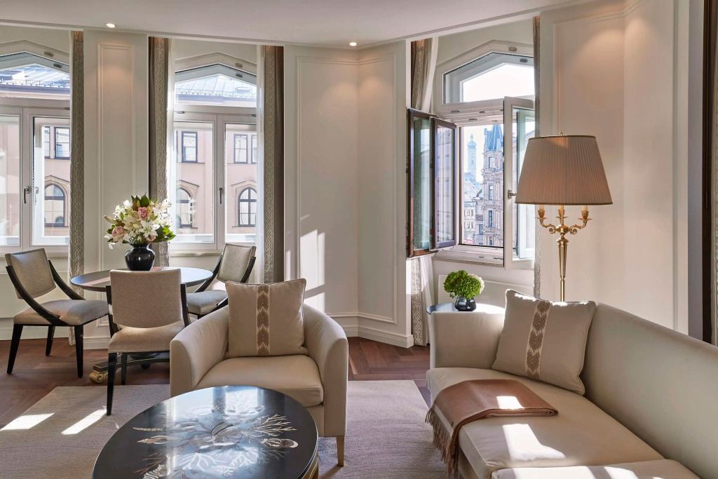Heller Wohnraum mit Sitzgelegenheiten und Blick auf die Stadt in der Signature Suite des Hotel Vier Jahreszeiten Kempinski München