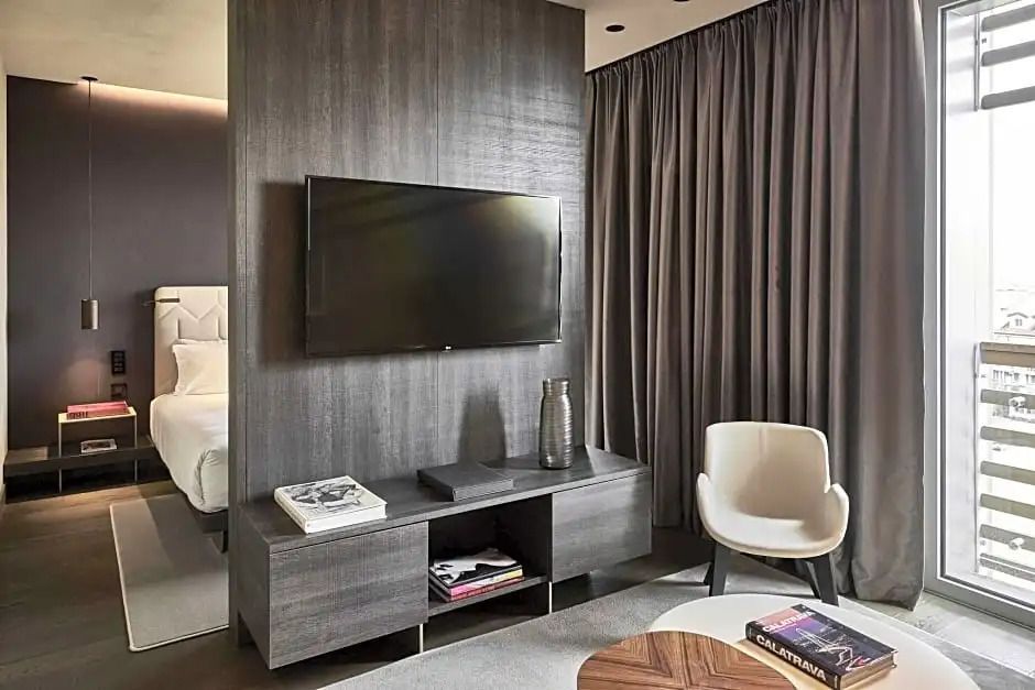 Modernes Hotelzimmer mit Flachbildfernseher, Sessel und dunklem Vorhang