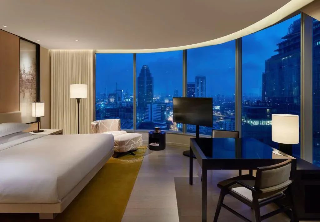 Luxuriöses Hotelzimmer mit Panorama-Fenster und Blick auf die Stadt bei Nacht.