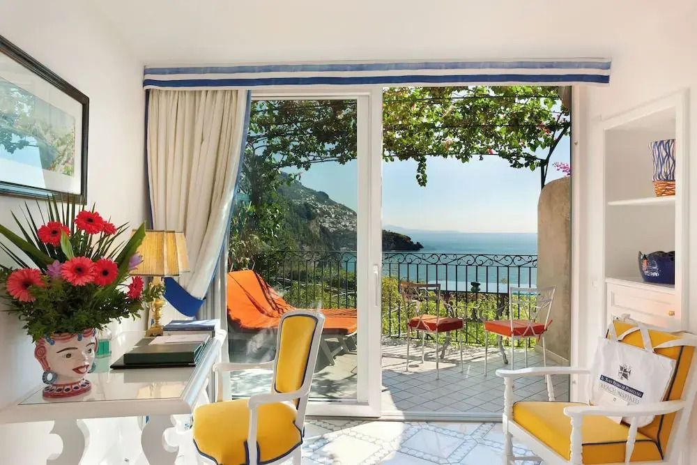 Terrasse mit Sitzgelegenheit und Blick aufs blaue Meer durch große Schiebetüren.