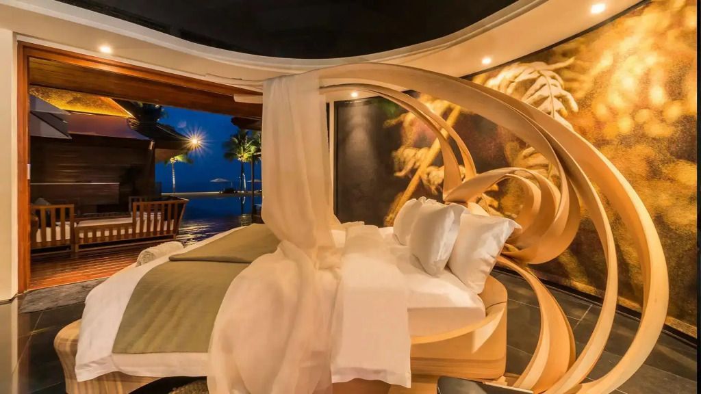 Gemütliches Schlafzimmer bei Nacht mit Blick auf den beleuchteten Poolbereich und das Meer.