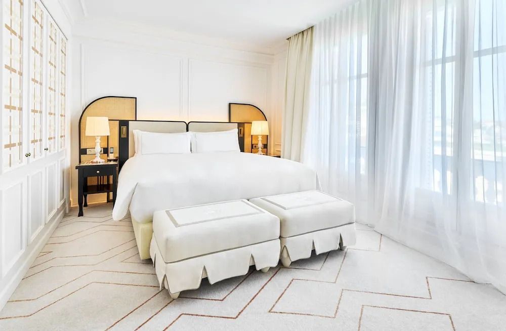 Elegantes Hotelzimmer mit Doppelbett, hellen Vorhängen und stilvollen Lampen.