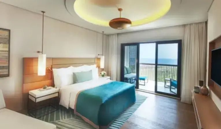 Geräumiges Hotelzimmer mit Doppelbett und Balkonblick auf den Garten und das Meer.
