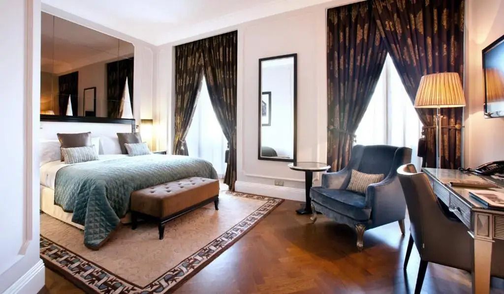 Elegantes Doppelzimmer mit dunklen Vorhängen, Sessel und Hartholzboden