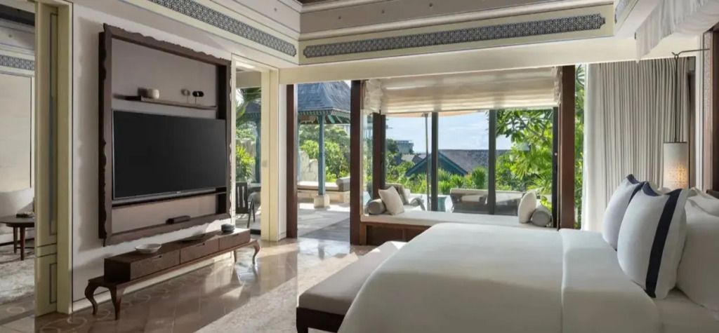 Helles Schlafzimmer mit großem Bett und Blick auf tropische Gartenlandschaft.