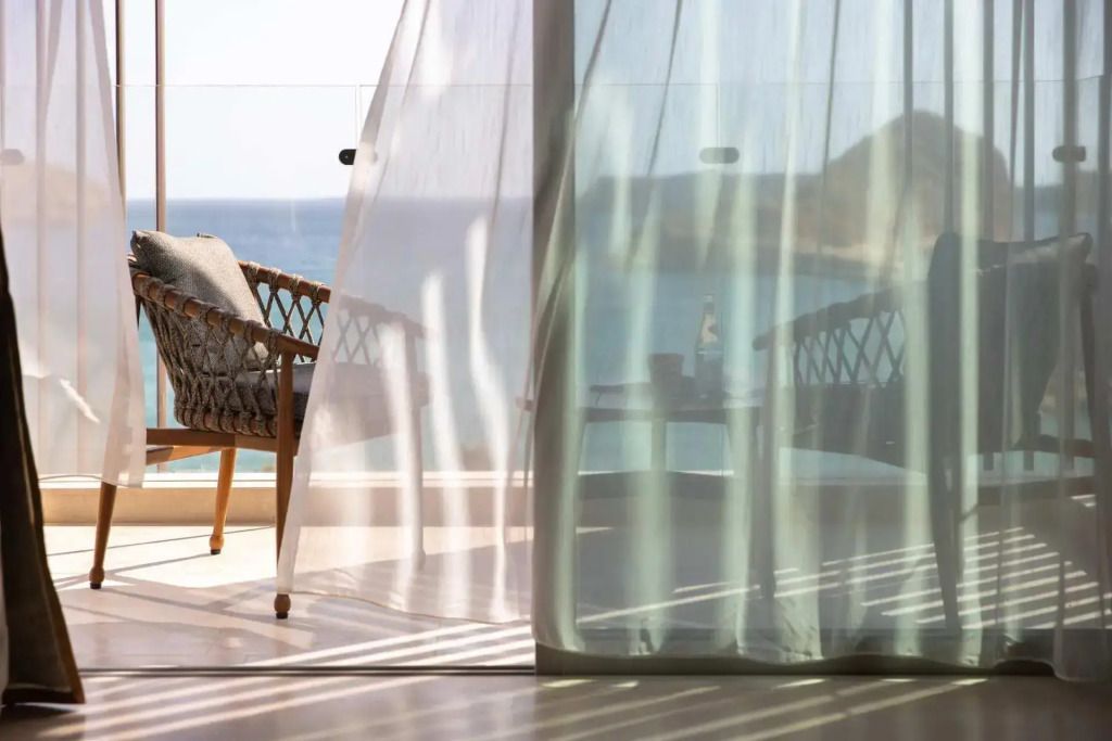 Blick auf das Meer vom Balkon mit luftigem Vorhang und stilvollem Stuhl.
