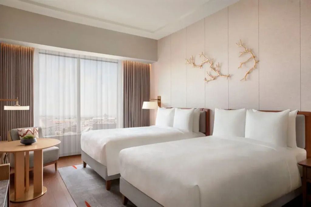 Elegantes Hotelzimmer mit zwei Doppelbetten und Stadtblick durch großes Fenster