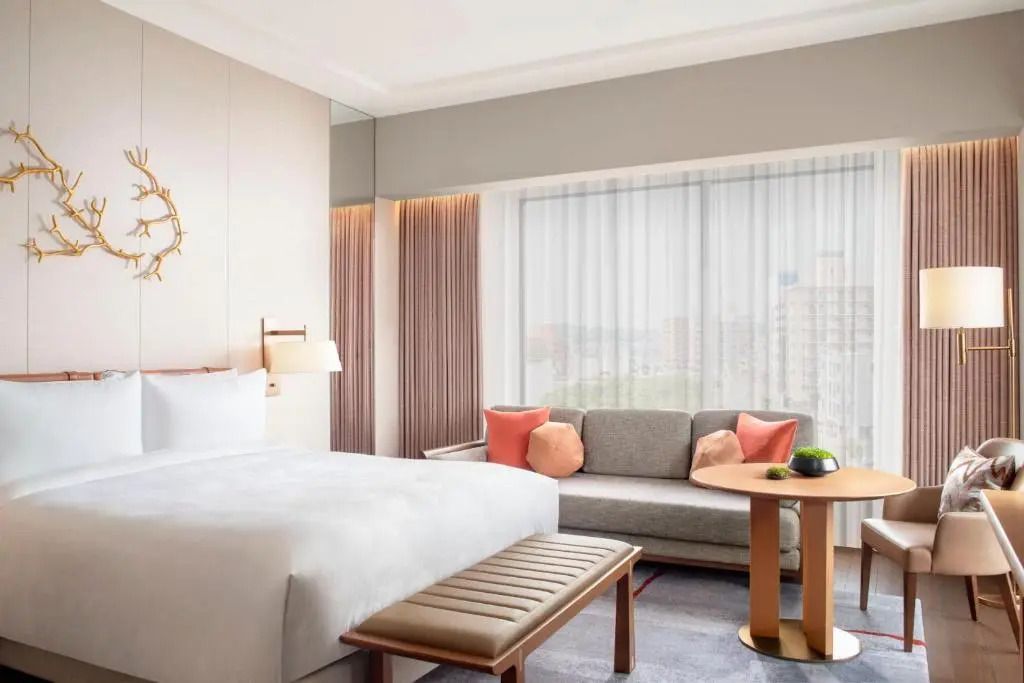 Luxuriöse Suite mit komfortablem Bett, Sitzbereich und Stadtansicht durch großes Fenster