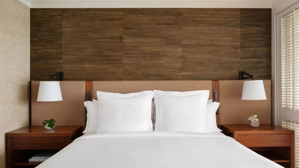 Elegantes Doppelbett mit weißen Kissen und Holzrückwand in der Resort Suite