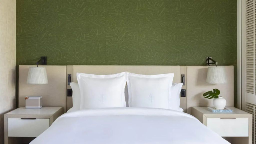 Elegantes Doppelbett mit weißer Bettwäsche in einem Resort Zimmer, grüne Wand als Hintergrund.