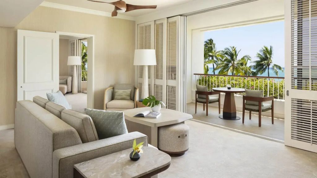 Wohnbereich mit Sitzgruppe und Balkon mit Meerblick in der Sunset Suite des Four Seasons Oahu.