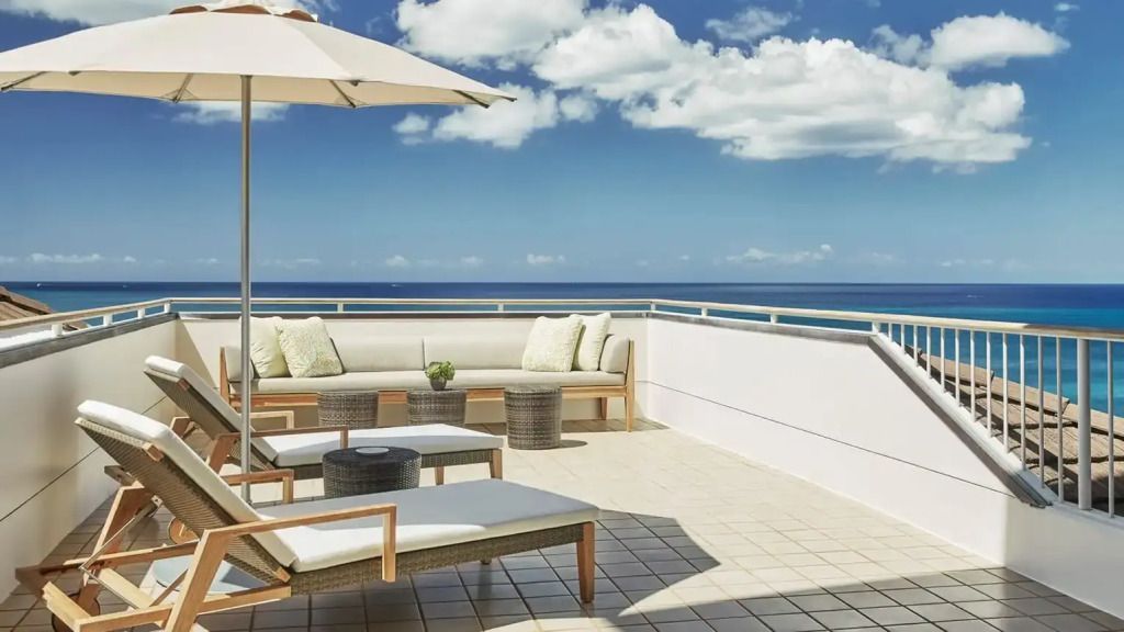 Privater Terrassenbereich mit Sonnenschirm und Sitzgelegenheiten, Meer und Wolken am Horizont.