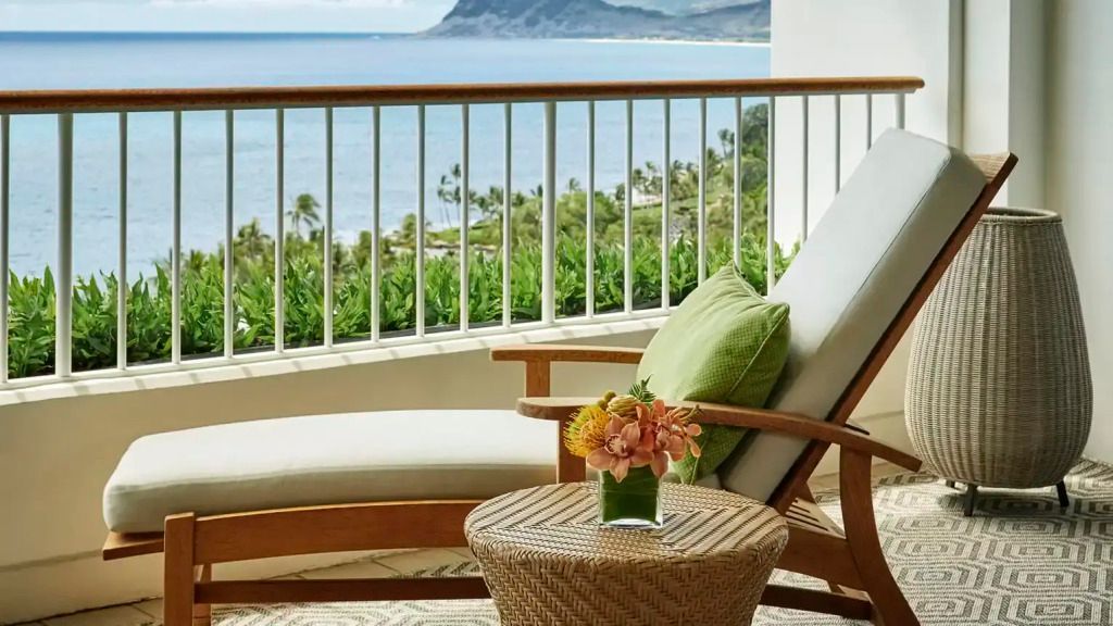 Liegestuhl mit Kissen auf Terrasse, Blick auf Ozean und Berge im Hintergrund.