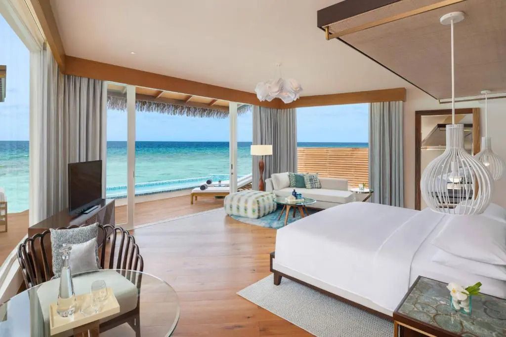 Blick aus einer Overwater Villa mit Doppelbett und Sitzecke auf das Meer