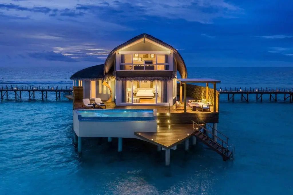 Overwater Villa bei Nacht mit beleuchtetem Pool und Terrasse über dem Wasser